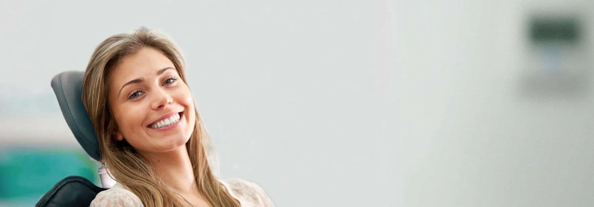A woman smiling while seated in a dentist's chair.