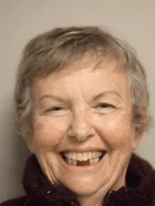 Smiling elderly woman with short hair wearing a dark jacket.