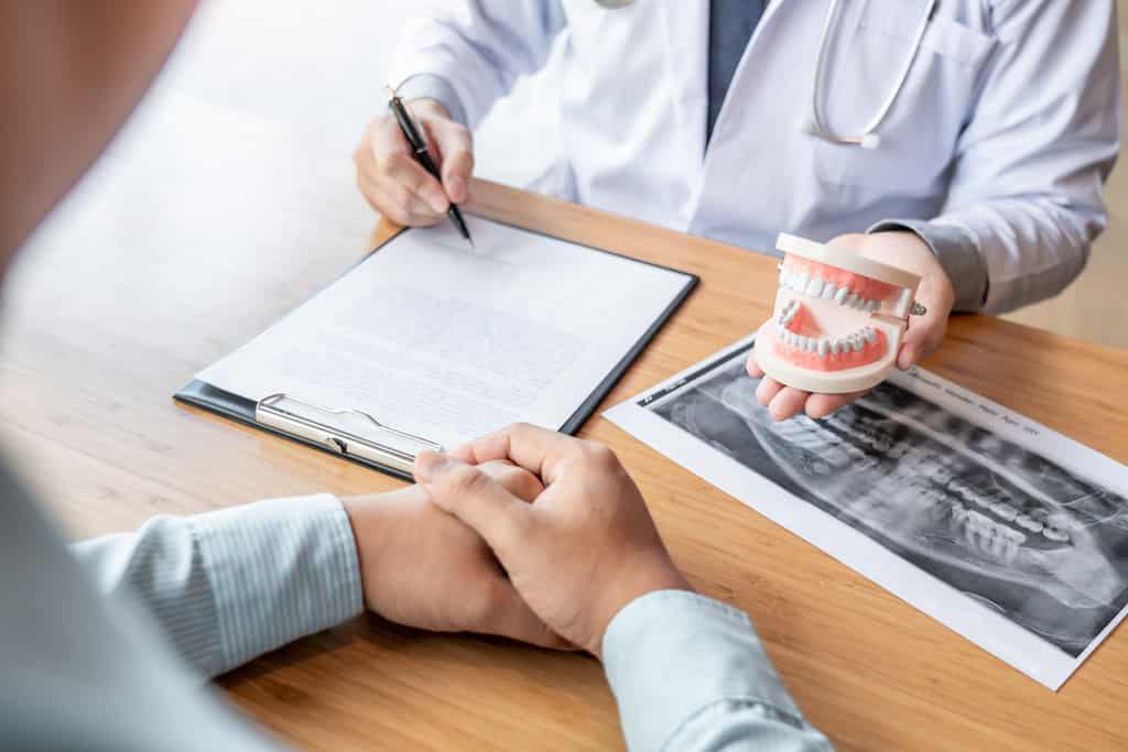 Dentist explaining dental procedure with model and X-ray to patient.