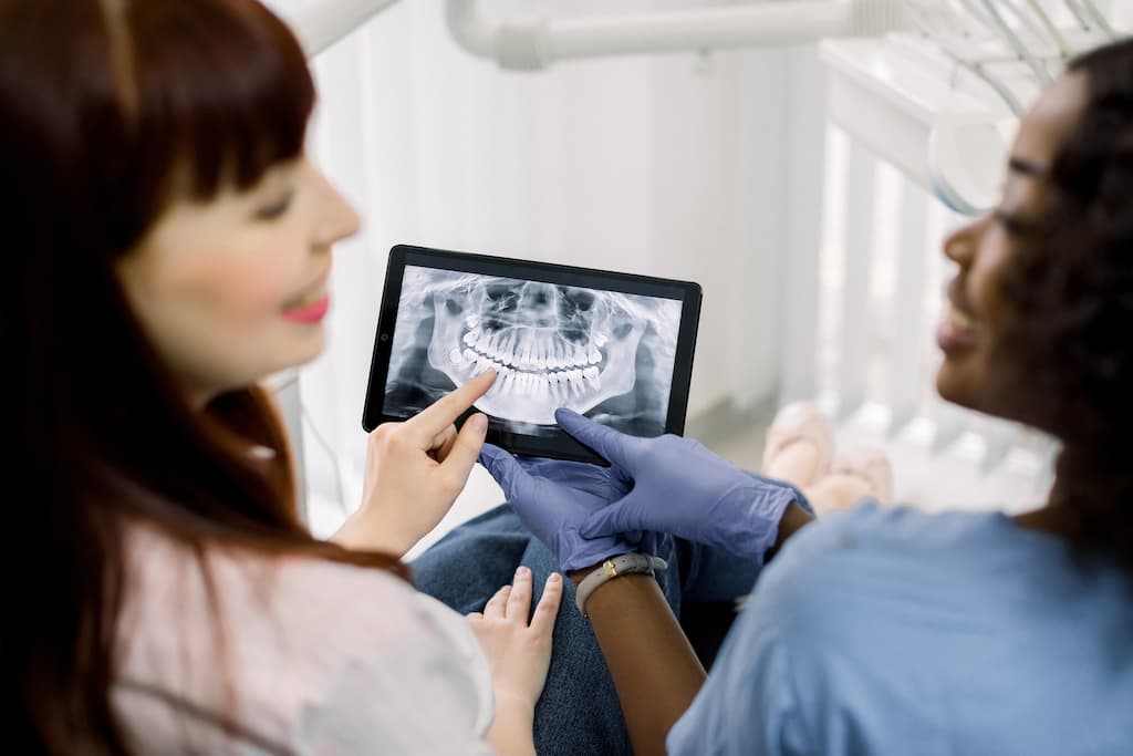 A dentist and patient review a dental X-ray on a tablet.