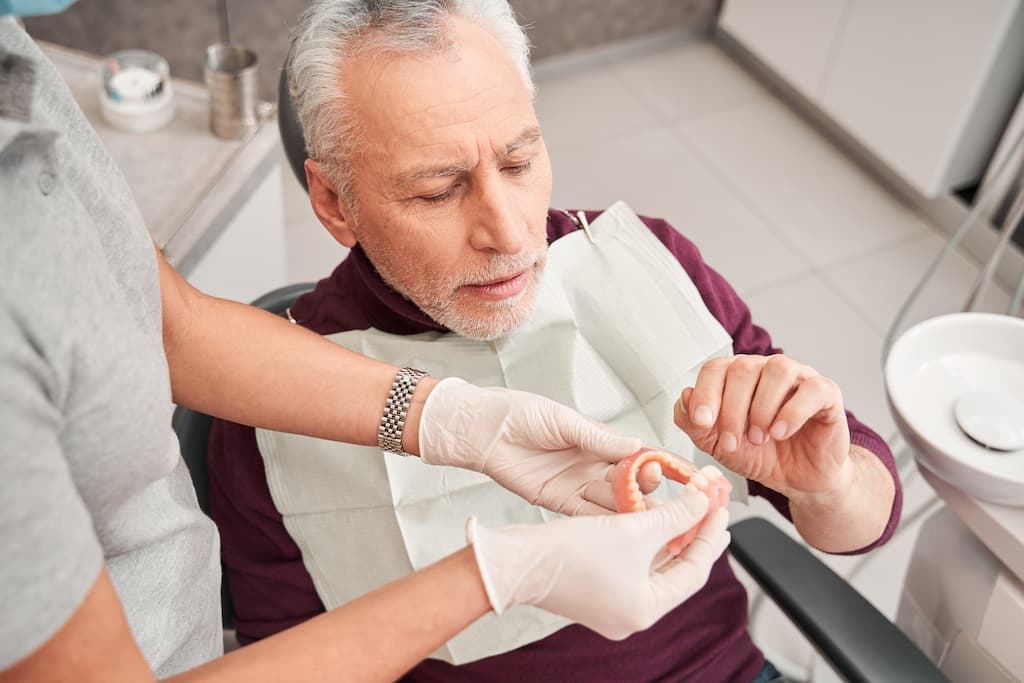A man examines a set of dentures held by a dental professional.