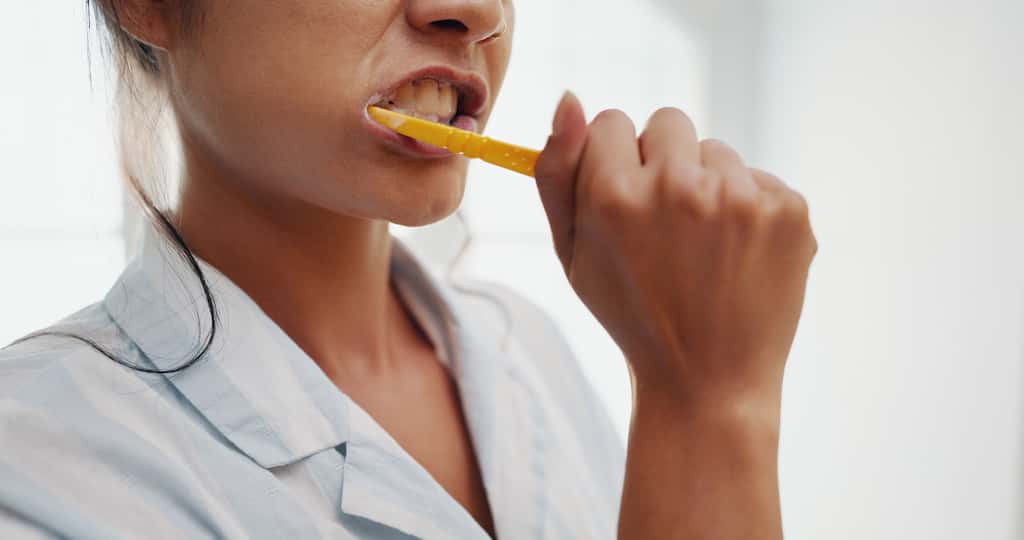 Person brushing their teeth with a yellow toothbrush.